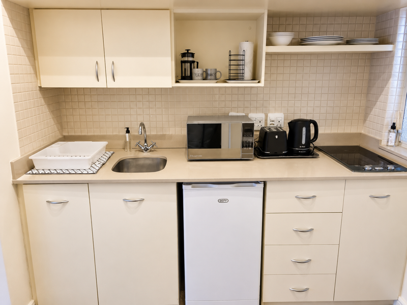 Compact kitchen featuring cream cabinetry, tiled backsplash, integrated induction hob, and stainless steel sink with ample under-counter storage.