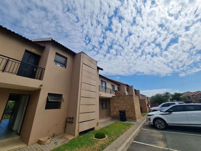 Exterior view of a multi-story apartment complex featuring brick facade, balcony access, and paved parking area.