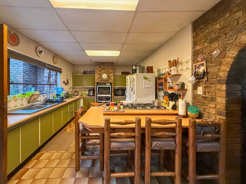 Spacious kitchen featuring a central breakfast island, built-in double oven, gas hob, and extensive cabinetry with a rustic exposed brick feature wall.