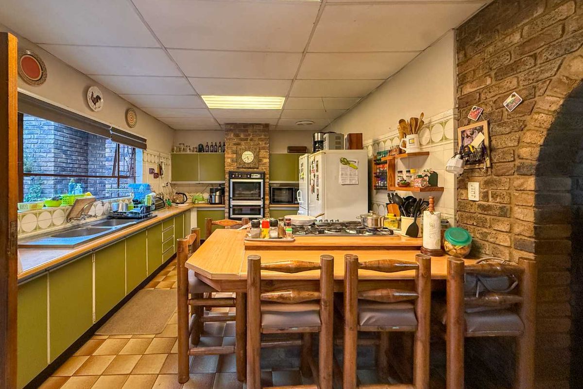 Spacious kitchen featuring a central breakfast island, built-in double oven, gas hob, and extensive cabinetry with a rustic exposed brick feature wall.
