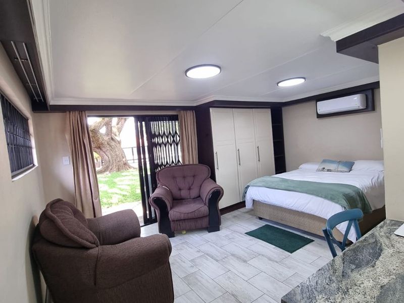 Open-plan bedroom and living area featuring tiled floors, built-in cupboards, air conditioning, and direct access to an outdoor space through a sliding glass door.
