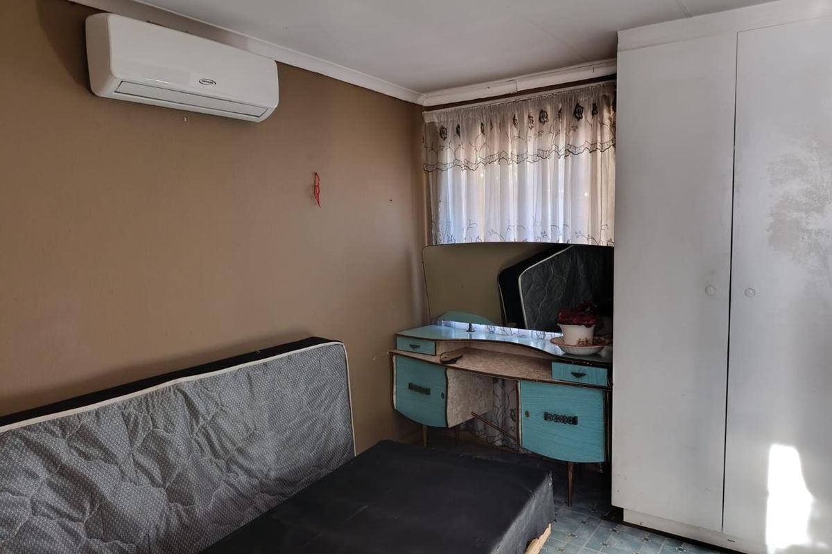 A bedroom featuring a wall-mounted air conditioning unit, built-in wardrobe, and tiled flooring, offering a functional space in need of cosmetic updates.