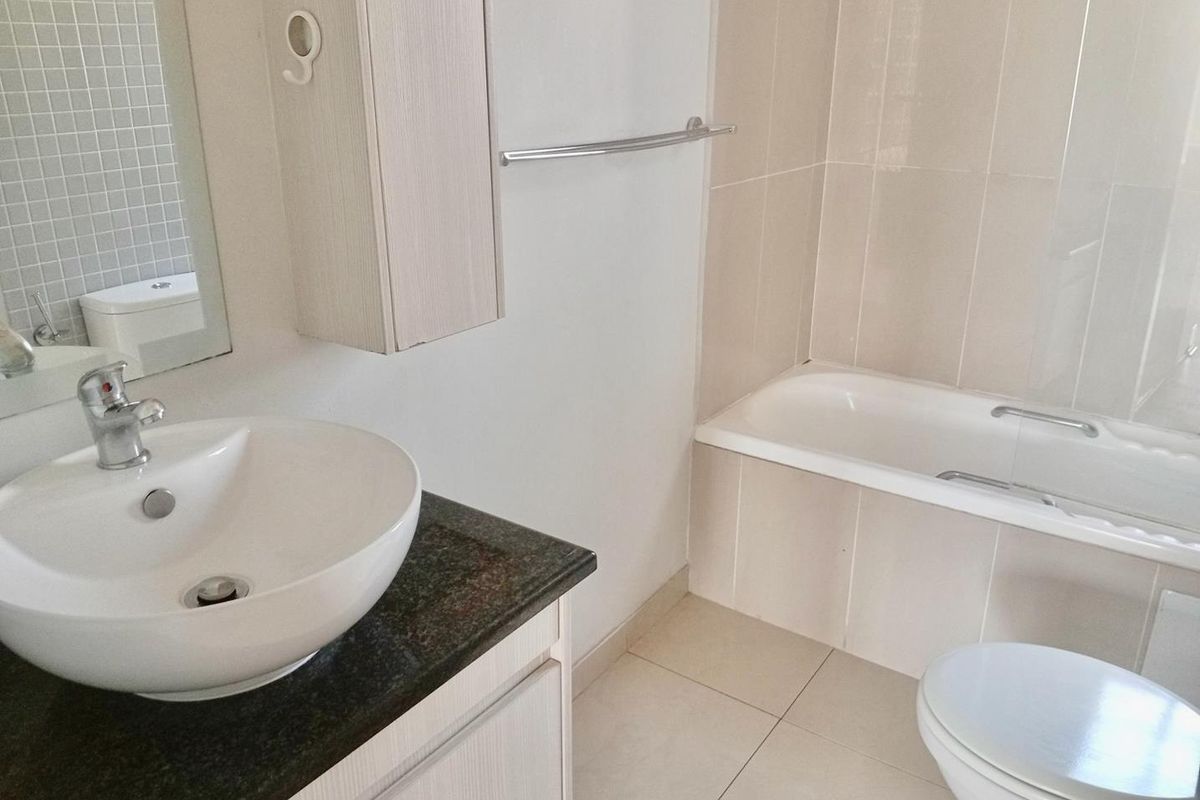 A clean, functional bathroom featuring a vessel sink on a granite vanity, a bathtub, and neutral wall tiling.