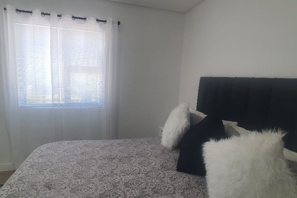 A bedroom featuring neutral walls, tiled flooring, and a window with fitted blinds, providing a simple and functional living space.