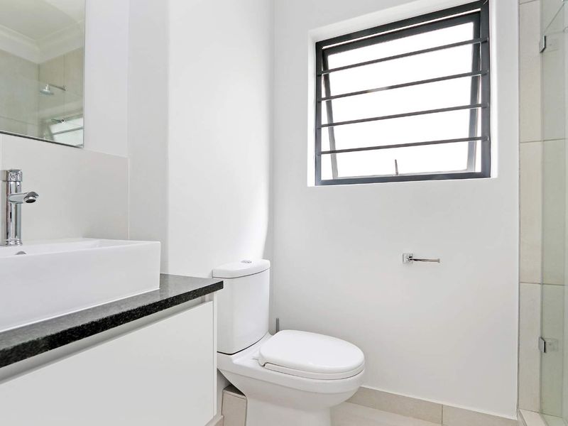 A modern, clean bathroom featuring a vessel sink on a granite vanity, a toilet, and a glass-enclosed shower with neutral tiling.