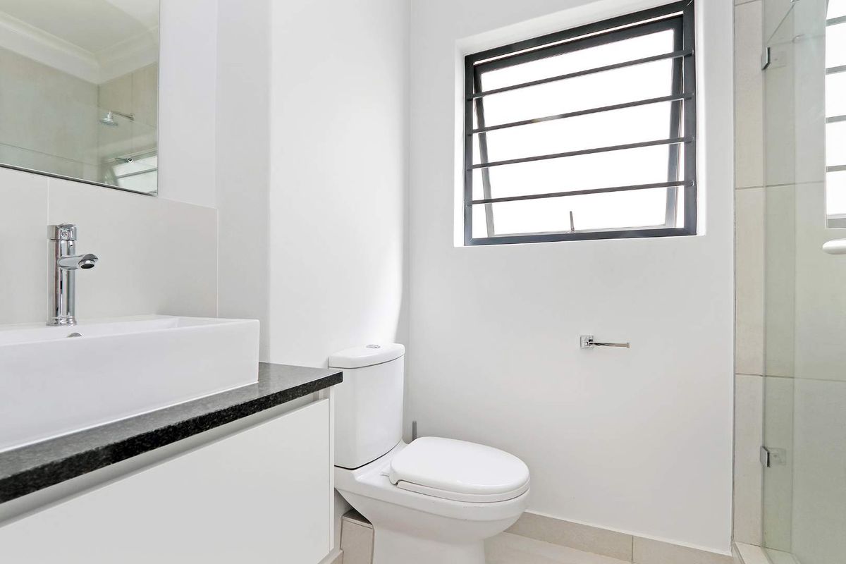 A modern, clean bathroom featuring a vessel sink on a granite vanity, a toilet, and a glass-enclosed shower with neutral tiling.