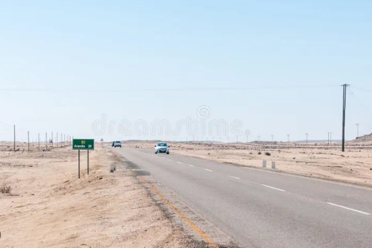 A view of a paved road passing through an arid, undeveloped landscape with utility poles and road signage visible.