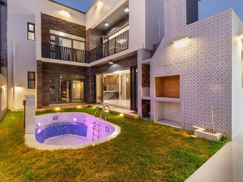 Modern rear courtyard featuring a built-in braai, a tiled plunge pool, and a multi-level architectural design with stone cladding and balcony access.