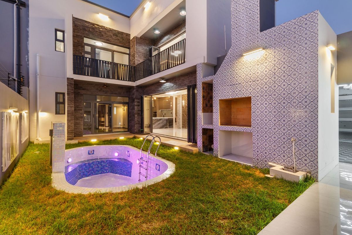 Modern rear courtyard featuring a built-in braai, a tiled plunge pool, and a multi-level architectural design with stone cladding and balcony access.