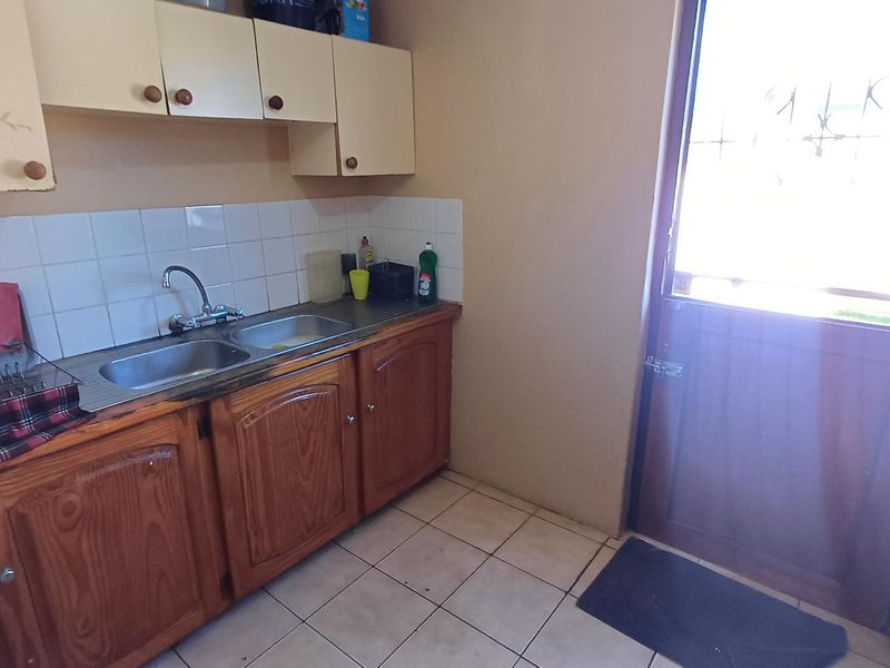 A functional scullery area featuring wooden cabinetry, a double stainless steel sink, tiled splashback, and direct access to the exterior via a security door.