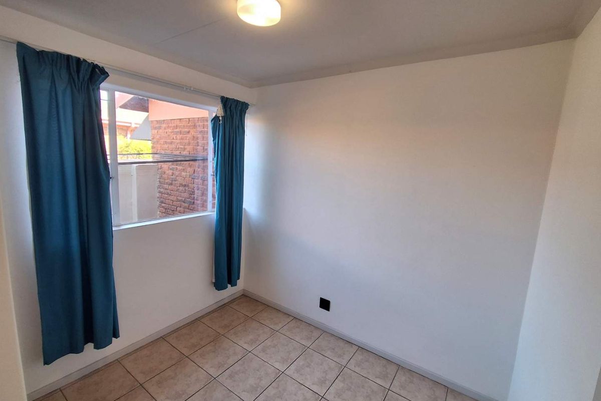 A clean, empty bedroom featuring neutral tiled flooring, white walls, and a window with blue curtains, providing a blank canvas for personalization.