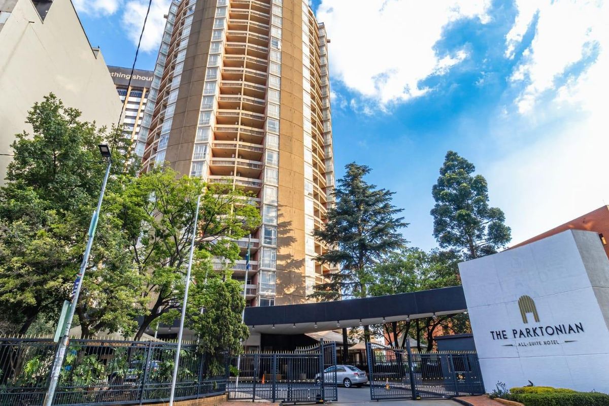 Exterior view of The Parktonian high-rise apartment building featuring a gated entrance, porte-cochere, and established landscaping.