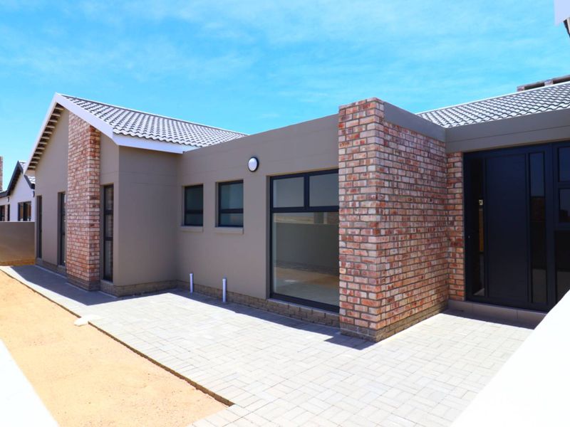 A modern rear exterior view of the house featuring brick accents, tiled roofing, and a paved patio area.