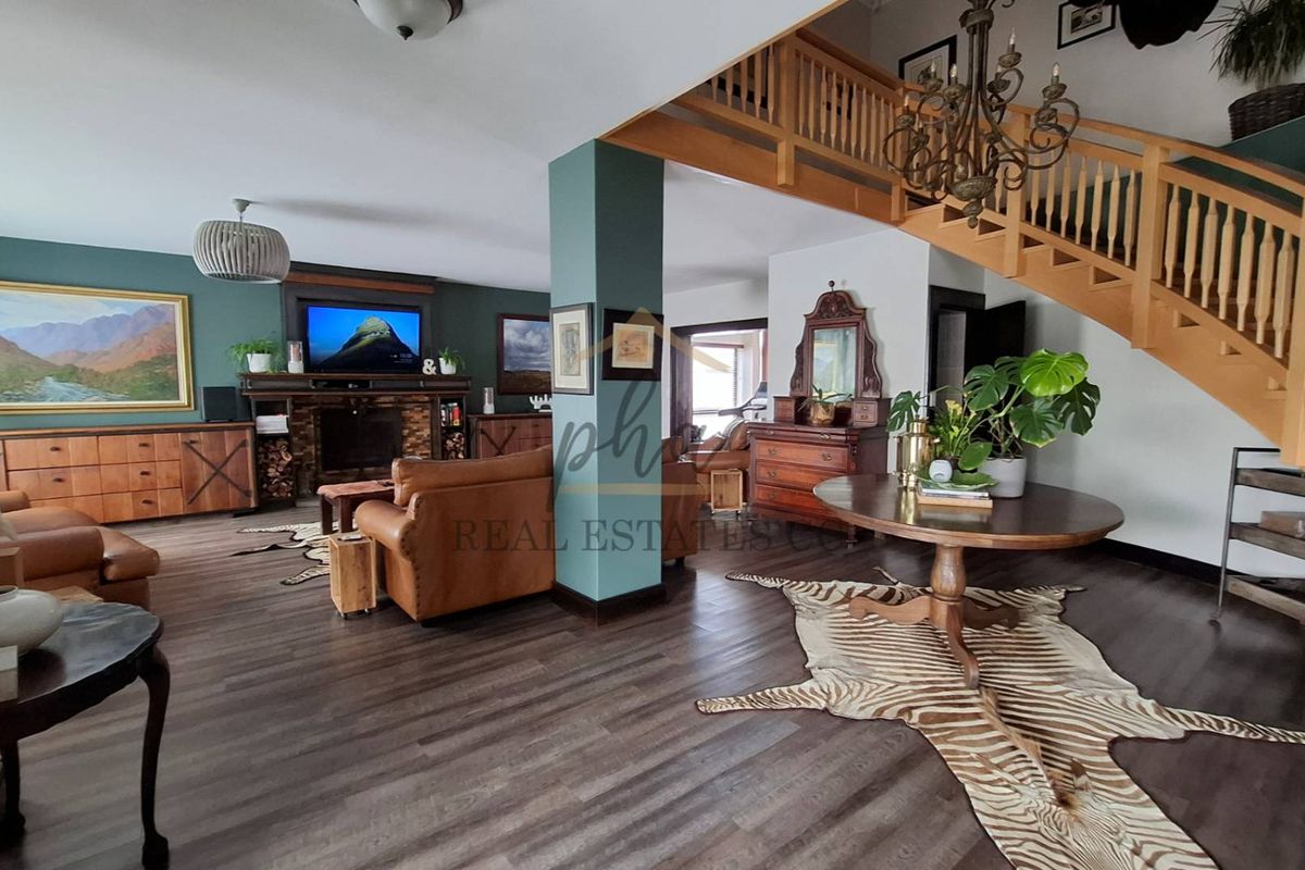 Spacious open-plan living area featuring a brick fireplace, dark laminate flooring, and a prominent wooden staircase with a matching balustrade.