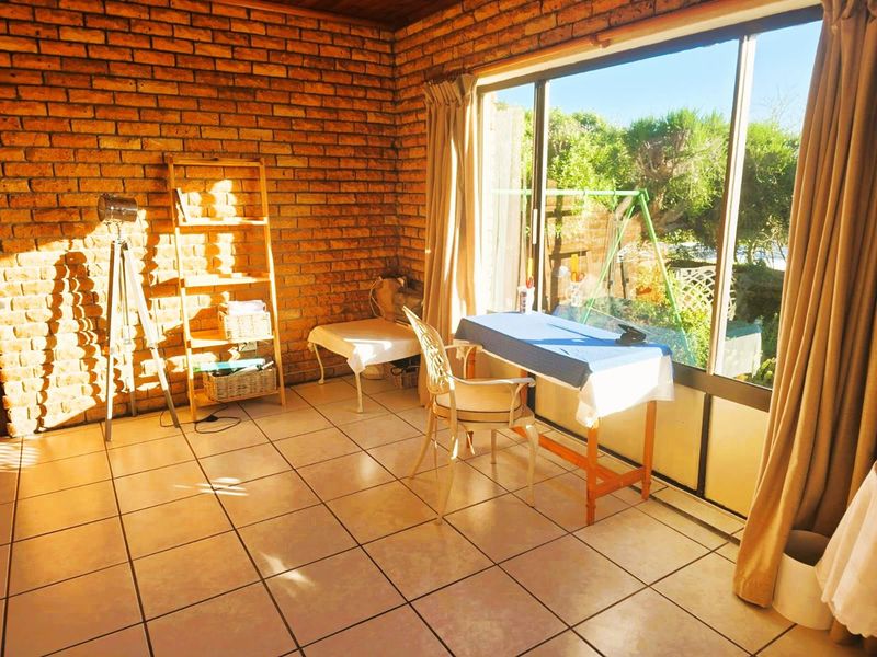 A sunlit living area featuring exposed brick walls, ceramic floor tiles, and a large sliding glass door providing access to the garden.