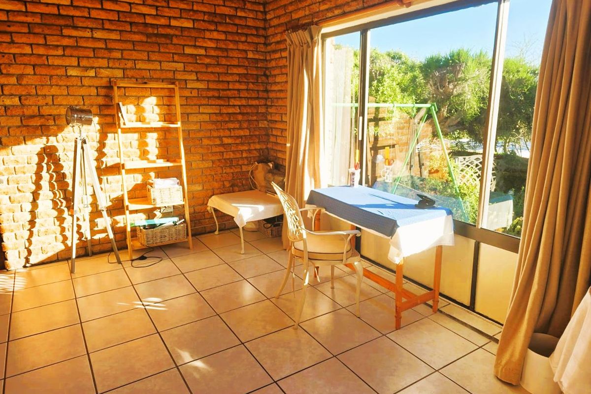 A sunlit living area featuring exposed brick walls, ceramic floor tiles, and a large sliding glass door providing access to the garden.