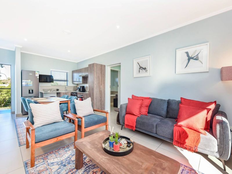 A bright open-plan living and kitchen area featuring modern cabinetry, tiled floors, and direct access to a balcony through a sliding glass door.