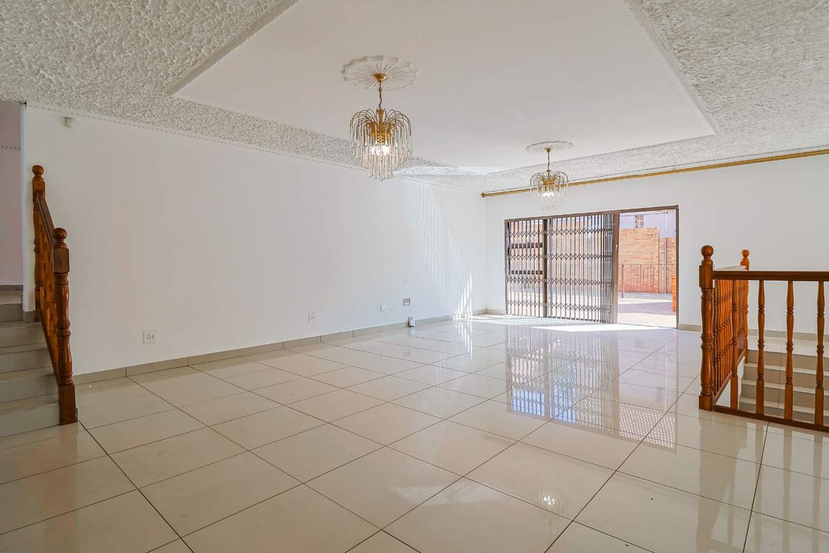 Spacious open-plan living area featuring polished floor tiles, decorative ceiling cornices, and a sliding door leading to an outdoor patio.