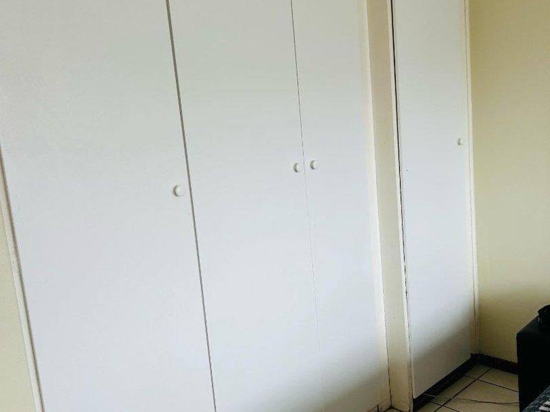 A bedroom featuring white built-in cupboards with ample storage space and tiled flooring throughout.