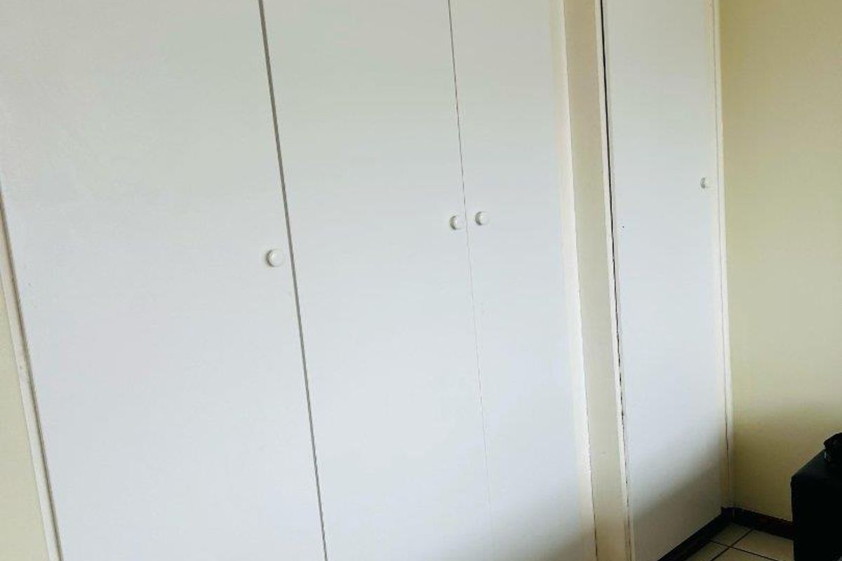 A bedroom featuring white built-in cupboards with ample storage space and tiled flooring throughout.