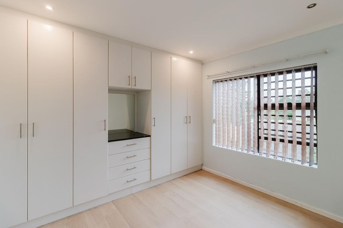 A bright bedroom featuring extensive floor-to-ceiling built-in cabinetry with integrated vanity and light wood-look flooring.