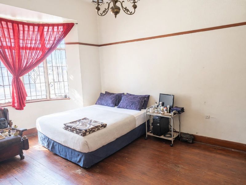 A bedroom featuring original hardwood flooring, a classic picture rail, and large windows with security bars, offering a traditional aesthetic.