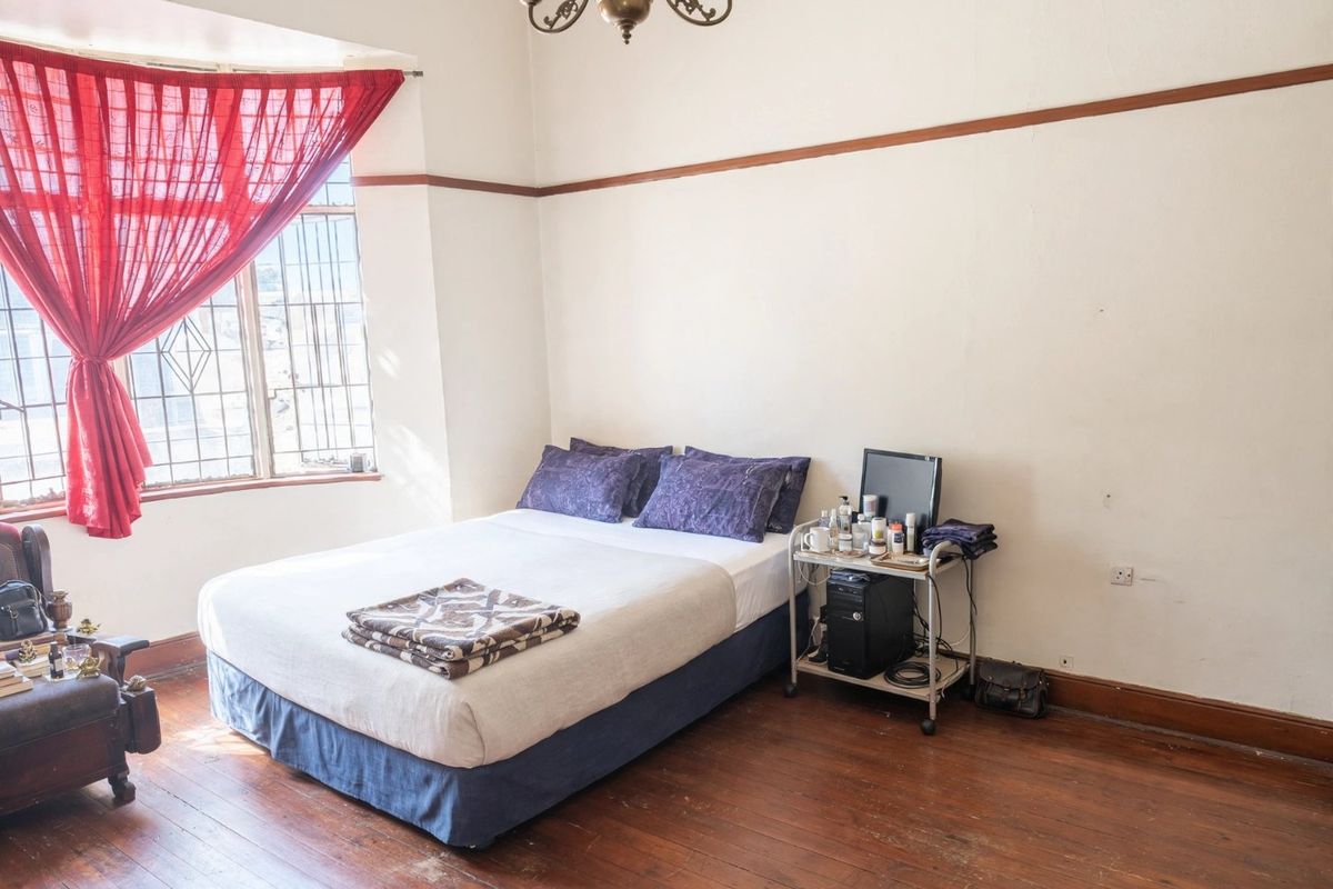 A bedroom featuring original hardwood flooring, a classic picture rail, and large windows with security bars, offering a traditional aesthetic.