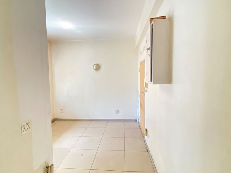A vacant, tiled hallway featuring a wall-mounted distribution board and basic lighting, presenting a blank canvas for interior updates.