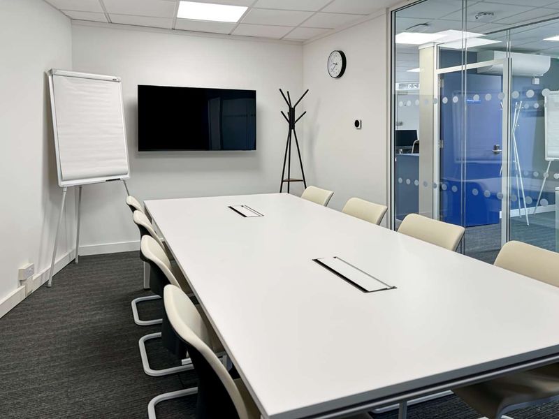 A modern, well-maintained office meeting room featuring a large conference table, glass partition walls, and professional carpet flooring.