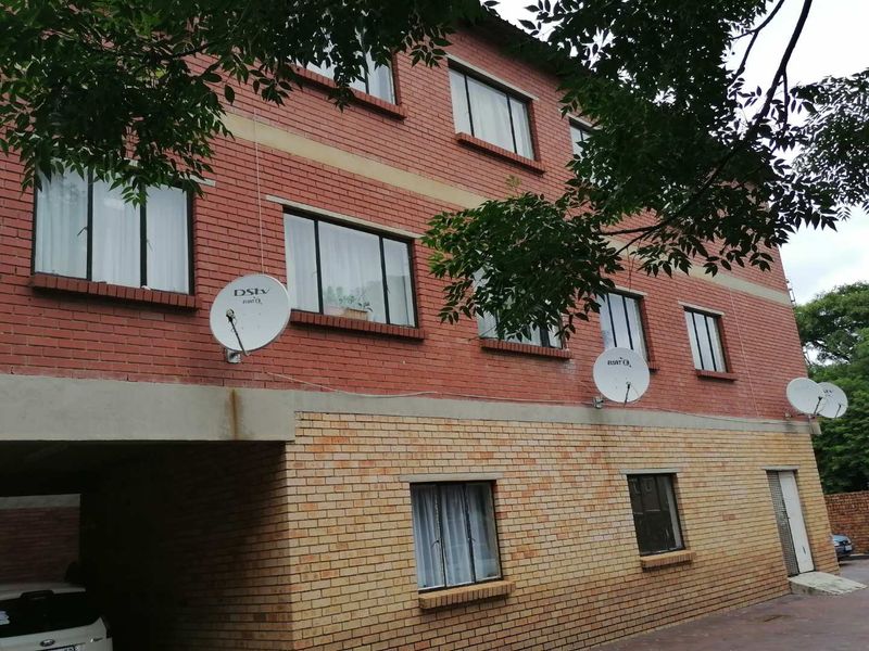 Exterior view of a multi-story apartment building featuring a face brick facade, multiple satellite dishes, and a covered ground-level parking area.