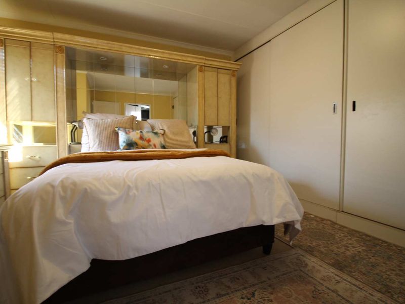 A bedroom featuring a large built-in wardrobe and a mirrored headboard unit, providing ample storage and a classic aesthetic.