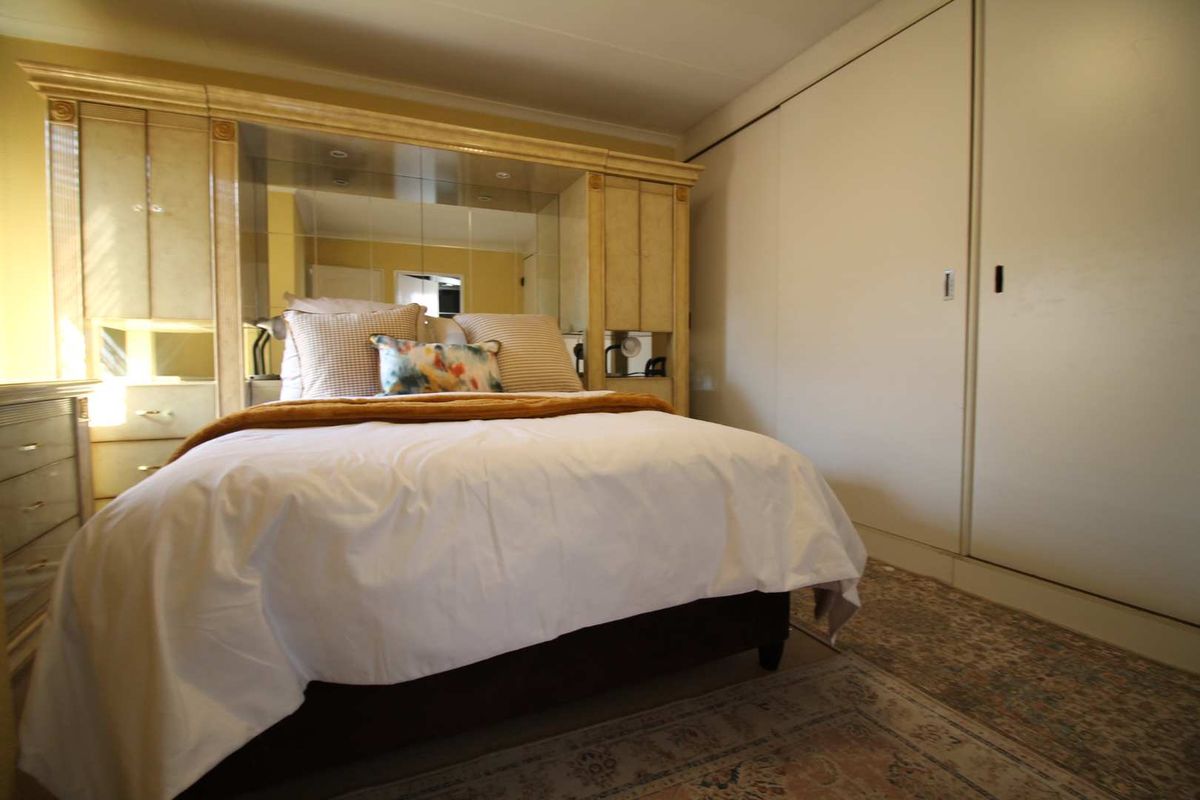 A bedroom featuring a large built-in wardrobe and a mirrored headboard unit, providing ample storage and a classic aesthetic.