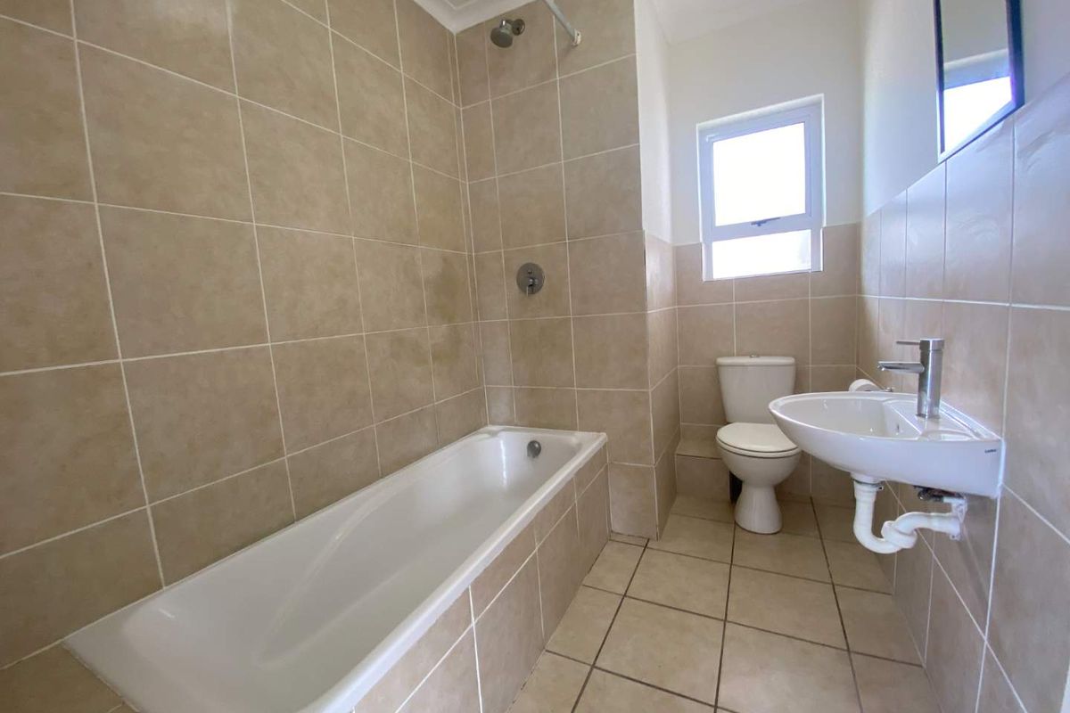 A functional bathroom featuring a built-in bathtub with shower head, a pedestal basin, and a toilet, finished with neutral ceramic wall and floor tiles.