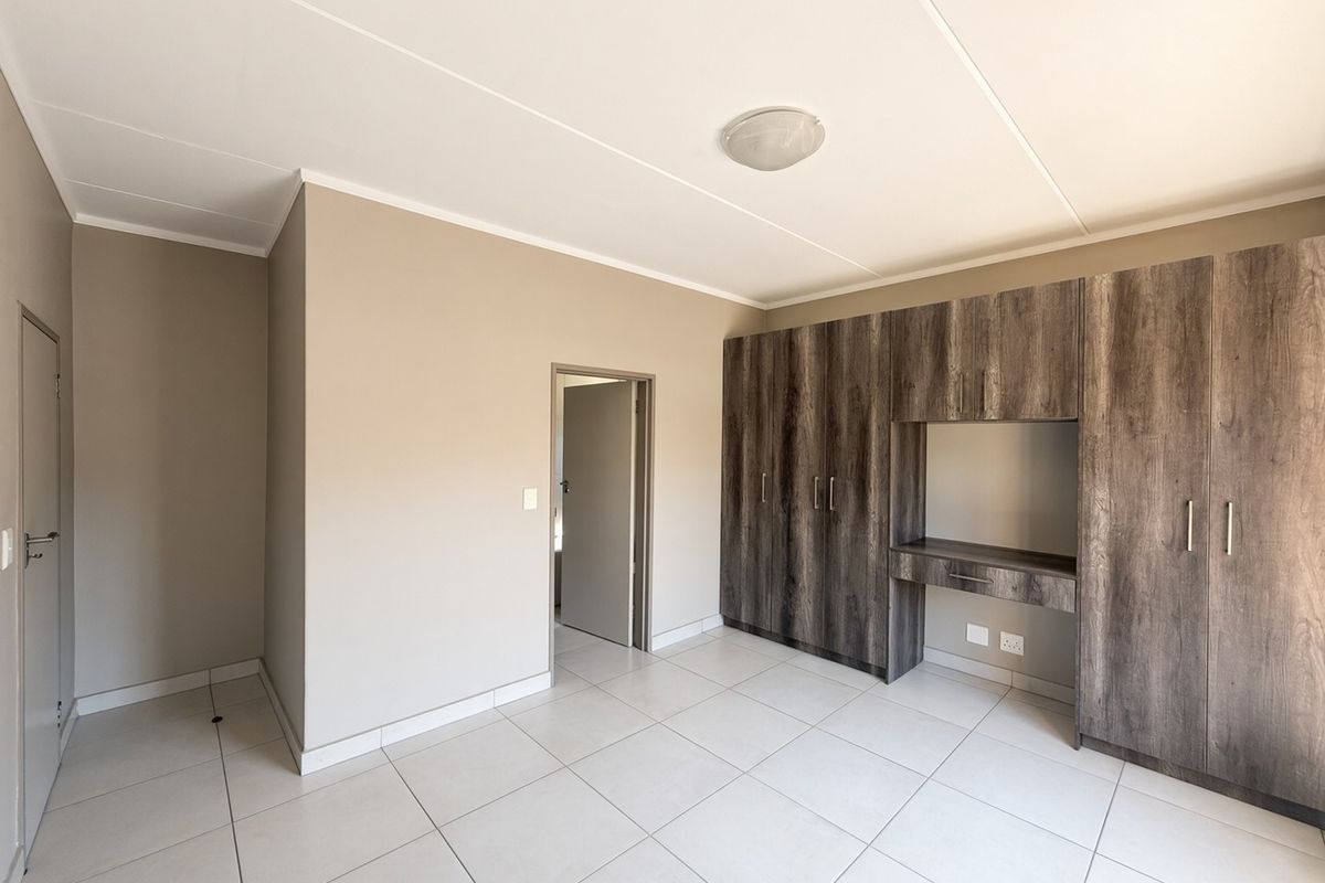 A clean, empty bedroom featuring neutral wall tones, modern tiled flooring, and extensive built-in wooden cabinetry with an integrated desk area.