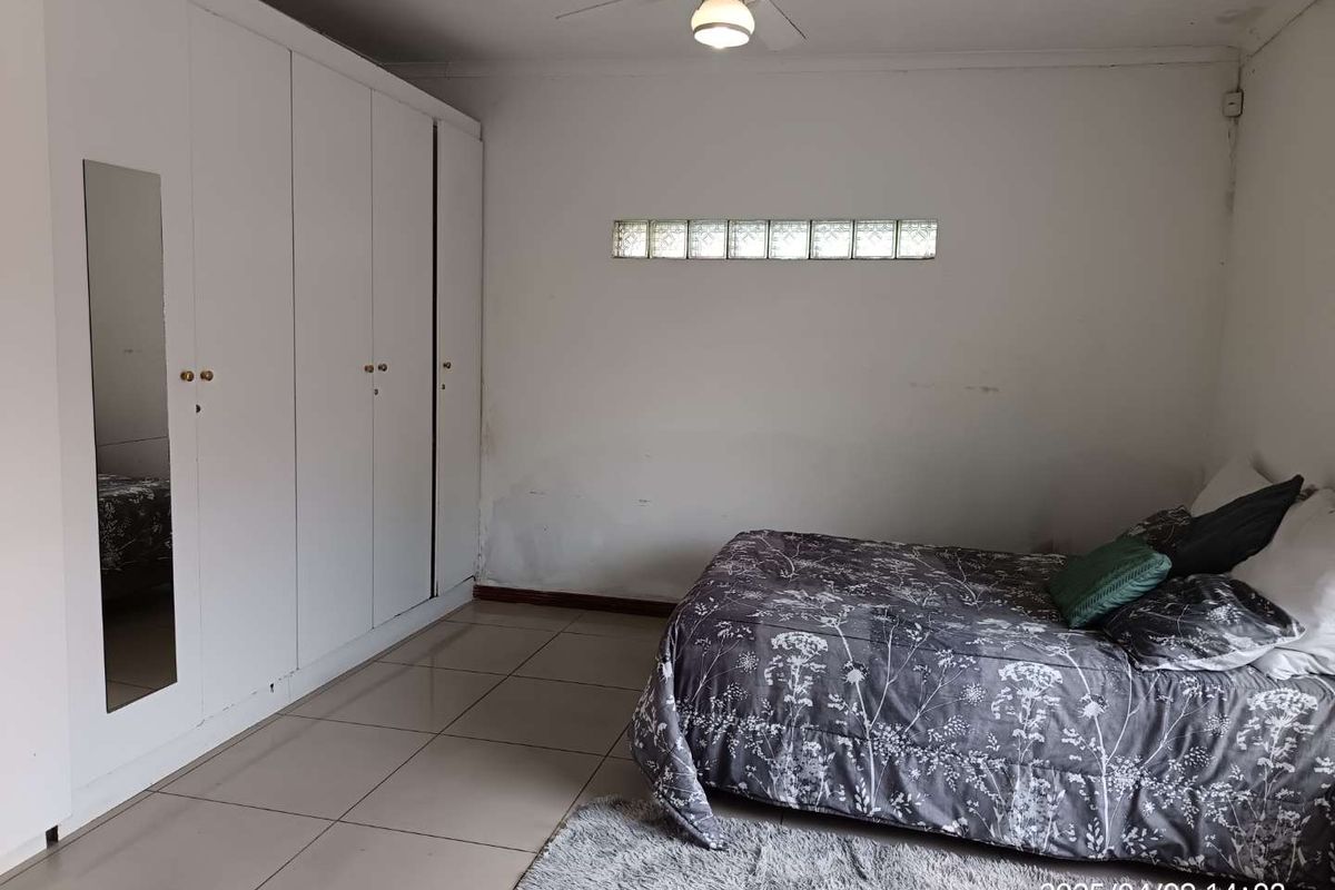 Bedroom featuring built-in floor-to-ceiling wardrobes, tiled flooring, and a horizontal glass block window for natural light.