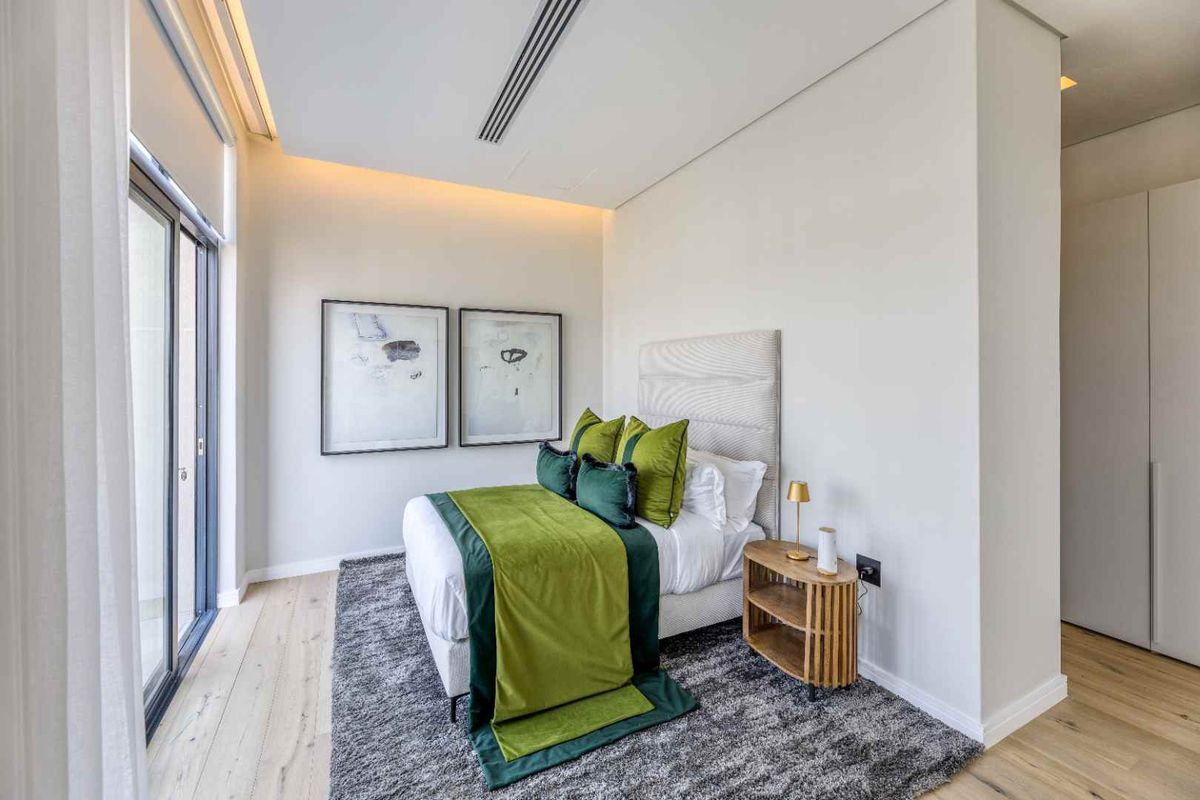 Modern bedroom featuring light timber flooring, recessed ceiling lighting, and large sliding glass doors providing access to the balcony.