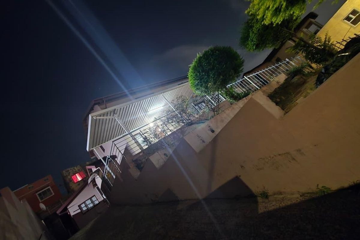 Night view of the rear exterior of the house, featuring a covered patio area, retaining wall, and metal safety railings.