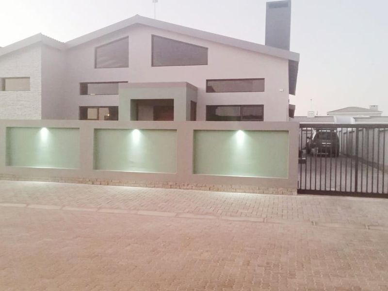 Modern front facade featuring a contemporary pitched roof design, integrated boundary wall lighting, and a secure metal driveway gate.