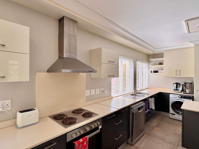 Modern kitchen featuring sleek cabinetry, built-in oven and hob, stainless steel extractor fan, and tiled flooring with integrated laundry space.