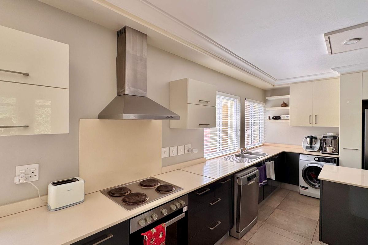 Modern kitchen featuring sleek cabinetry, built-in oven and hob, stainless steel extractor fan, and tiled flooring with integrated laundry space.