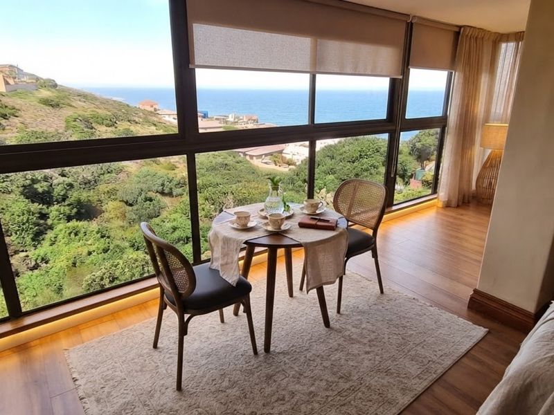 A bright living area featuring expansive floor-to-ceiling windows with panoramic coastal views, timber flooring, and integrated recessed floor lighting.