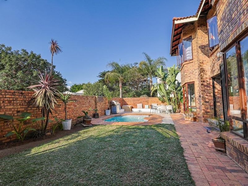 A private rear garden featuring a paved patio area, a small swimming pool, and a well-maintained lawn enclosed by face brick boundary walls.