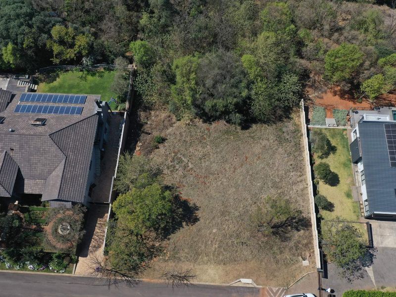 An aerial view of a vacant residential plot situated between two existing properties, featuring established trees and boundary walls.