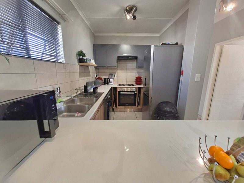 A functional kitchen featuring built-in cabinetry, stone countertops, a stainless steel double sink, and integrated cooking appliances including an oven and hob.