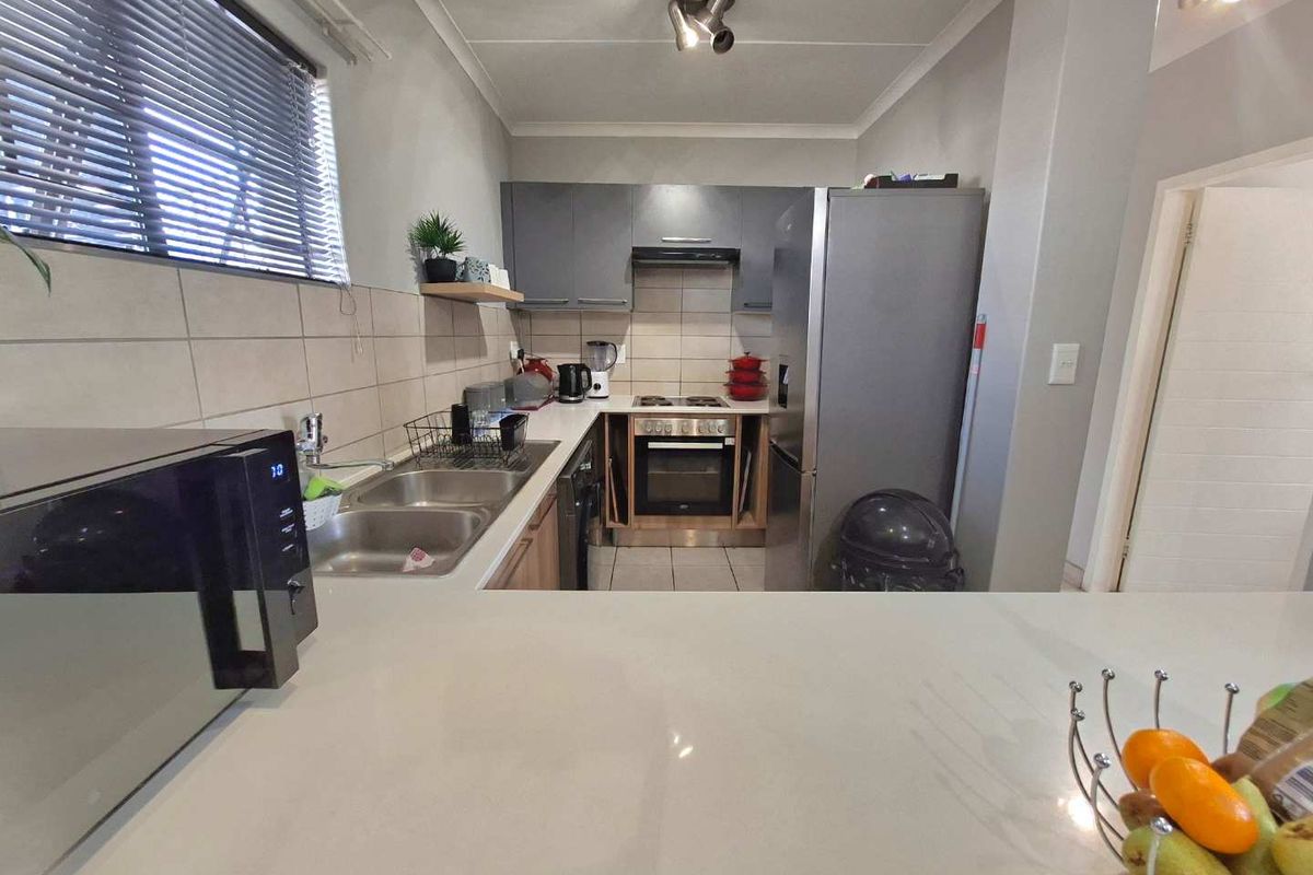 A functional kitchen featuring built-in cabinetry, stone countertops, a stainless steel double sink, and integrated cooking appliances including an oven and hob.