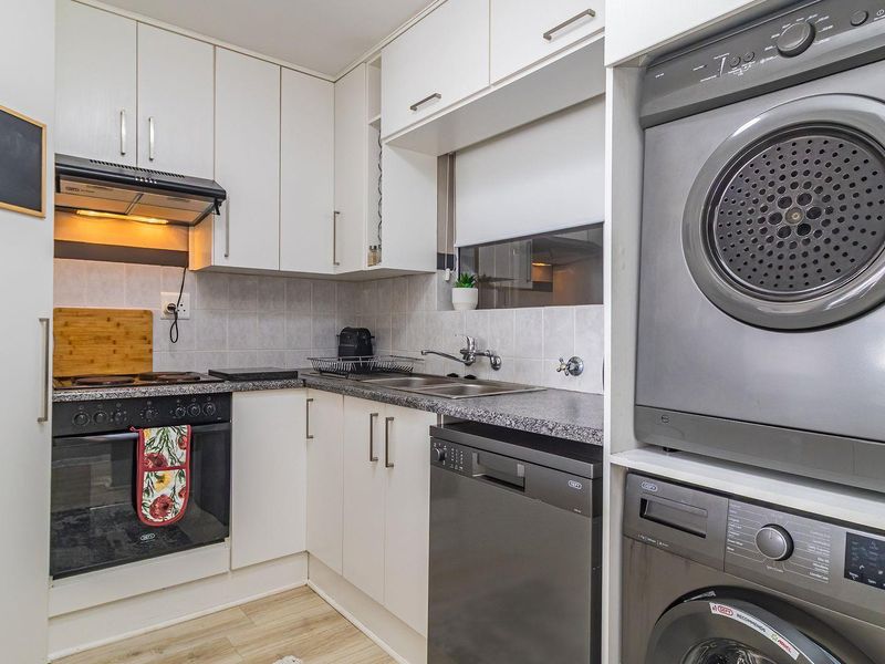 Compact kitchen featuring white cabinetry, granite countertops, tiled backsplash, and integrated appliances including an oven, hob, extractor fan, and dishwasher.