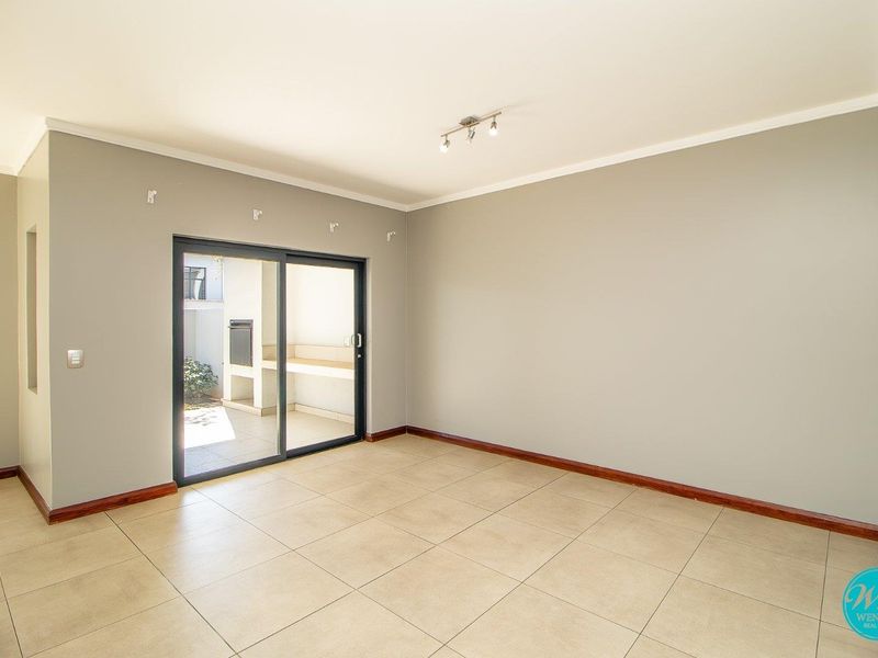 A bright, empty living room featuring neutral wall tones, tiled flooring, and a sliding glass door providing access to an outdoor patio area.