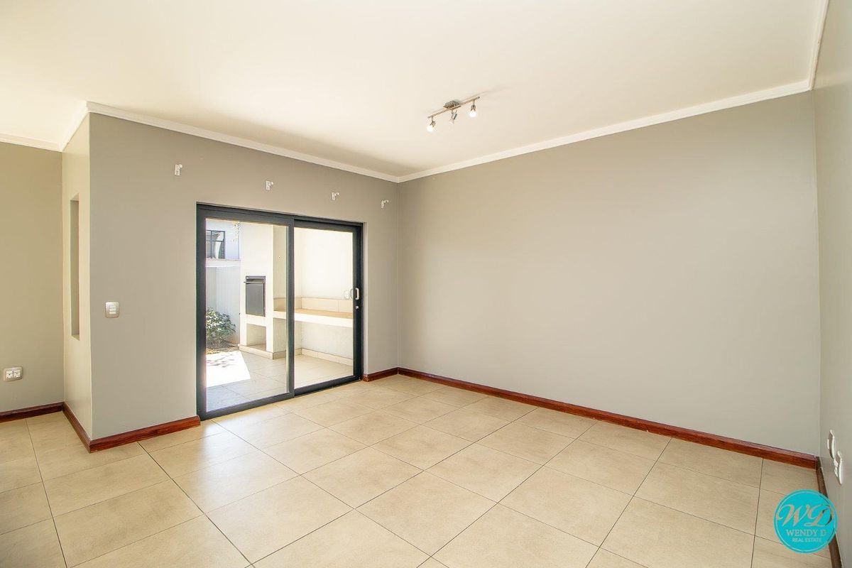 A bright, empty living room featuring neutral wall tones, tiled flooring, and a sliding glass door providing access to an outdoor patio area.