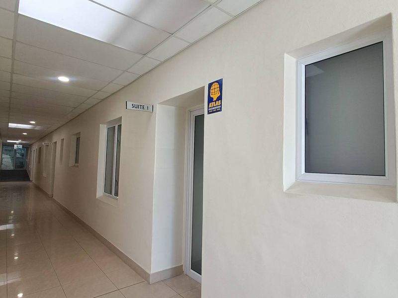 A clean, well-lit commercial office hallway featuring tiled floors, suspended ceilings, and multiple suite access points with frosted glass windows.