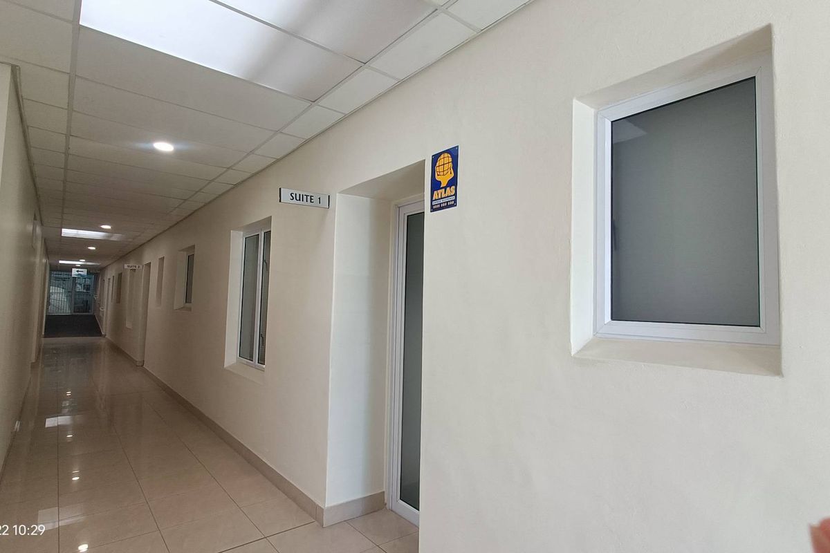 A clean, well-lit commercial office hallway featuring tiled floors, suspended ceilings, and multiple suite access points with frosted glass windows.